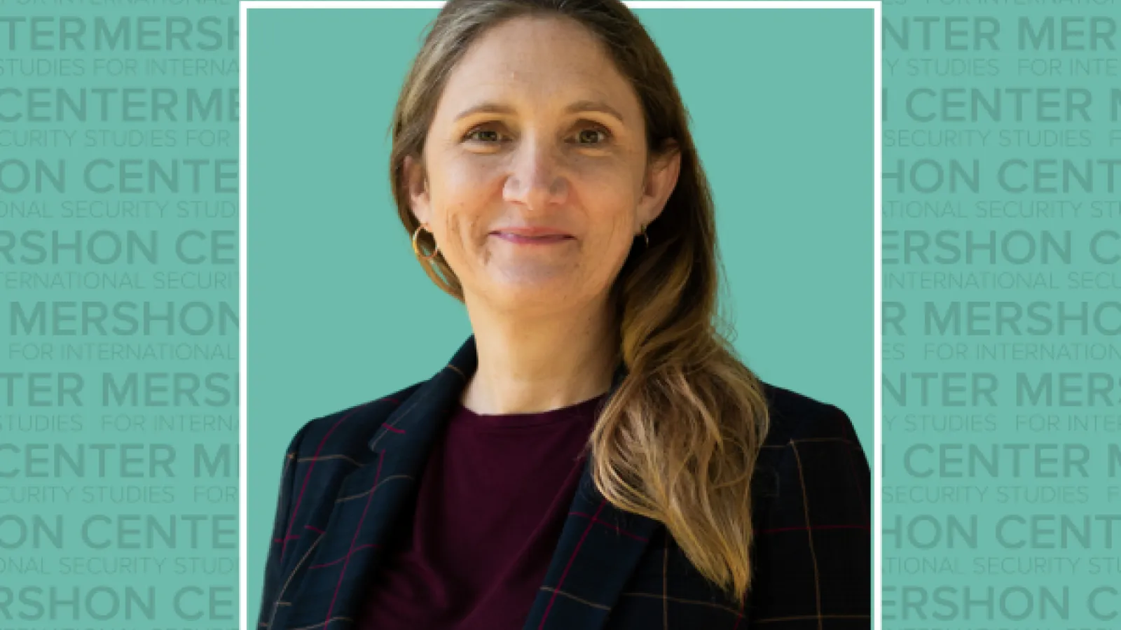 A photo of a woman with shoulder-length hair and a blazer, smiling in front of a turquoise background with the Mershon Center logo.