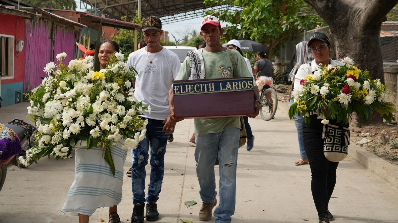 Family members carrying small coffin and flowers during burial ritual for a disappeared loved one
