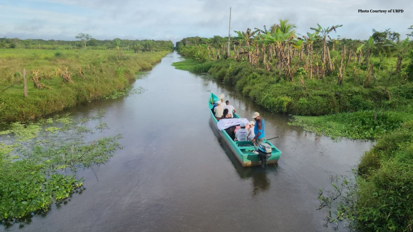Boat with people on a river between two green fields