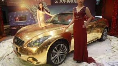Expensive gold car with women in dressers standing next to it