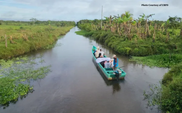 Boat with people on a river between two green fields