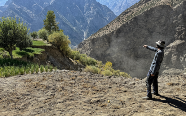 Man on hill points at rocky mountains