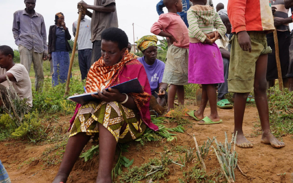 Girl in Africa journaling outside among a group of people