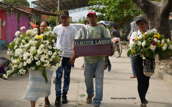Family members carrying small coffin and flowers during burial ritual for a disappeared loved one
