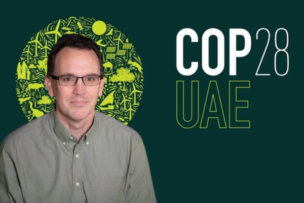 Photograph of a man in a green shirt with the logo for COP 28 UAE in green and yellow, indicating involvement or support for the climate change conference in the United Arab Emirates