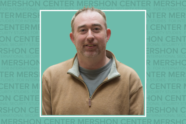 Photo of Brooks Marmon in a tan quarter zip sweater on a teal background that has repeating Mershon Center text.