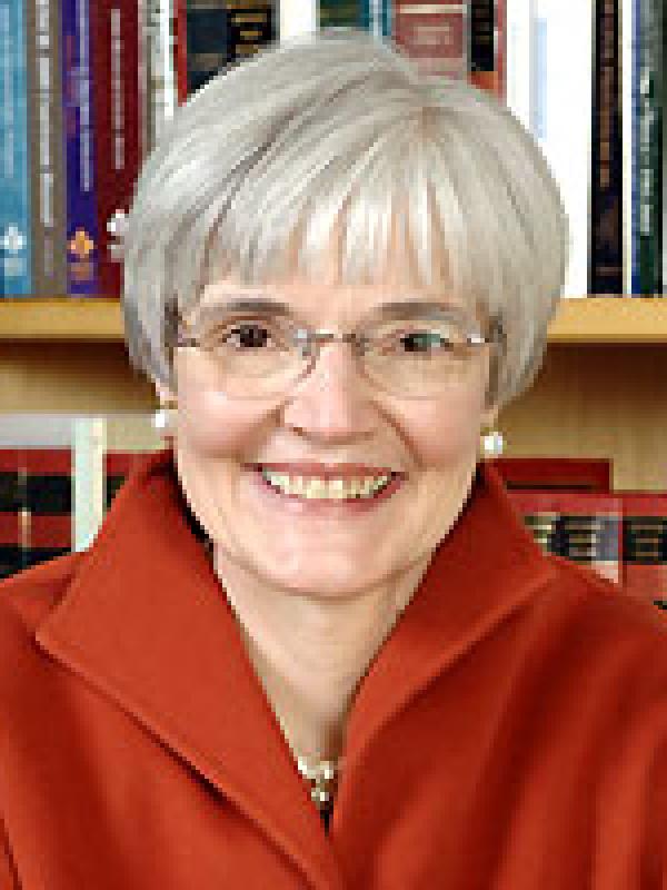 Photo of Nancy Rogers in front of a bookshelf in a red coat