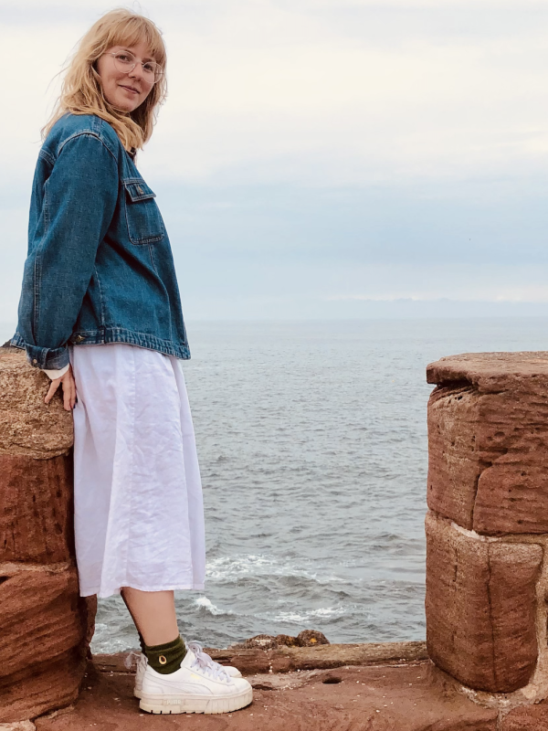 Victoria Paige smiling while standing near the edge of a rocky coastline. 